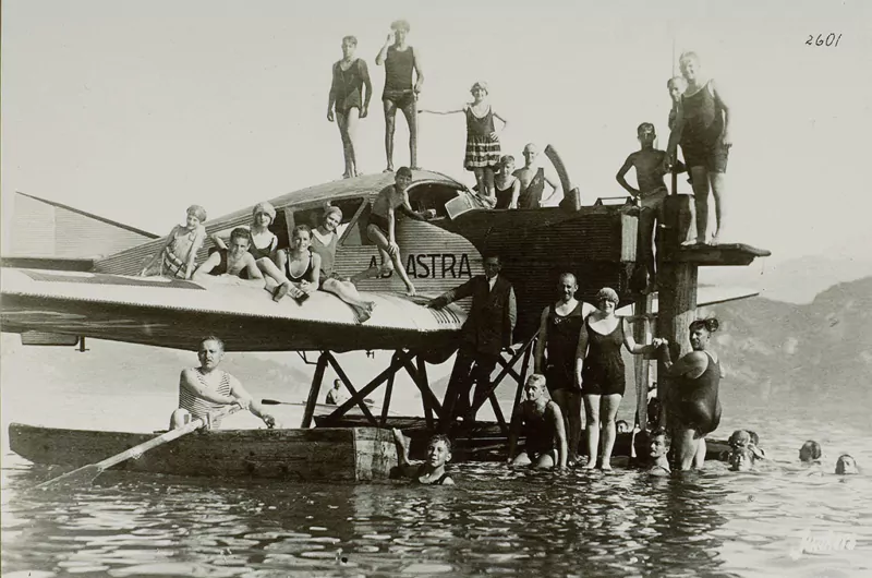 Eine historische Aufnahme eines Junkers F13 Flugzeugs, das auf dem Wasser steht und Menschen drumherum und schwimmen